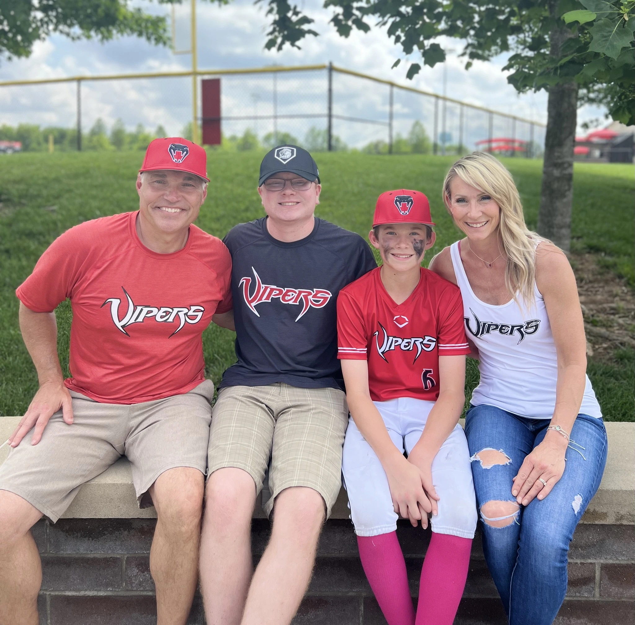 Pat Rigsby seated outdoors with family in baseball uniforms